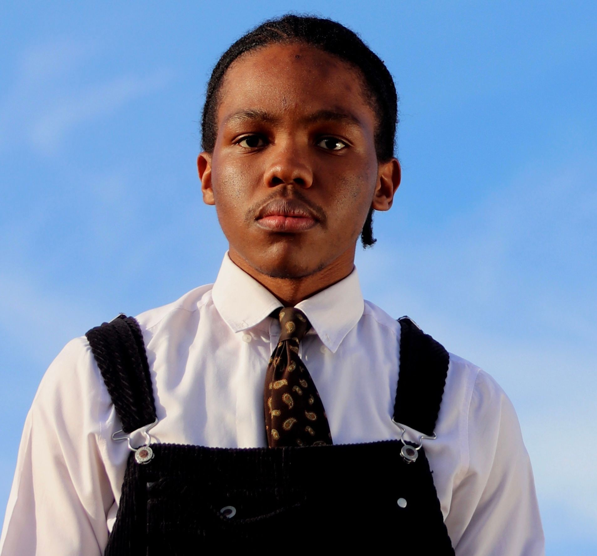 Person wearing a white shirt with patterned tie and dark suspenders against a blue sky background.